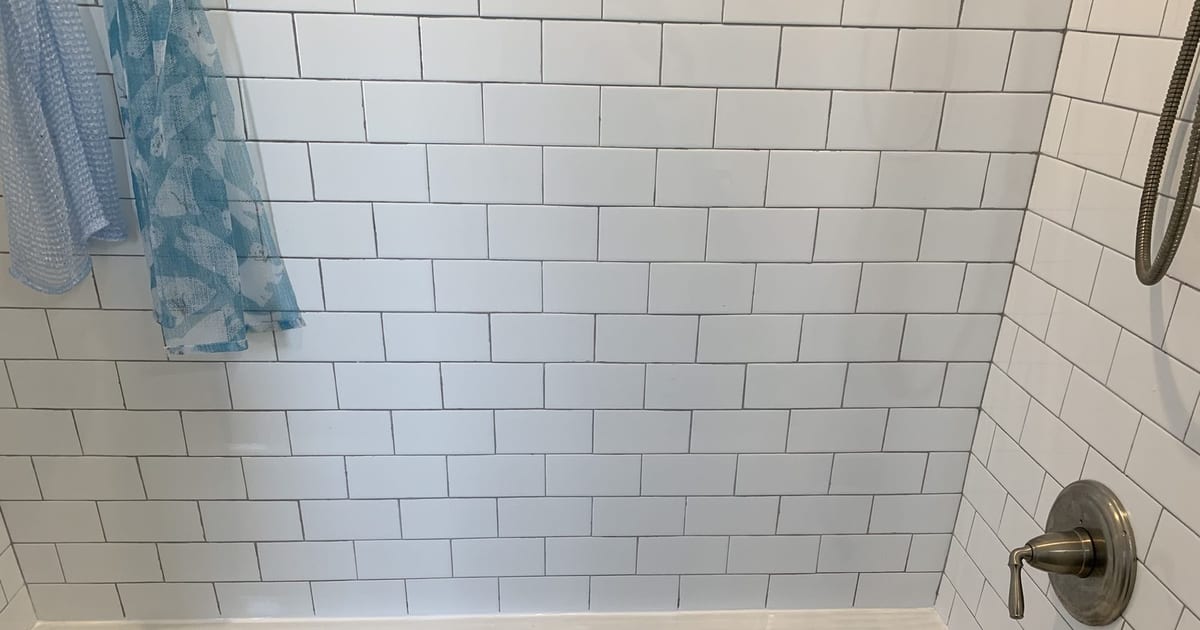 Shower and tub area with tiled surround and a shower head mounted on a flexible hose.