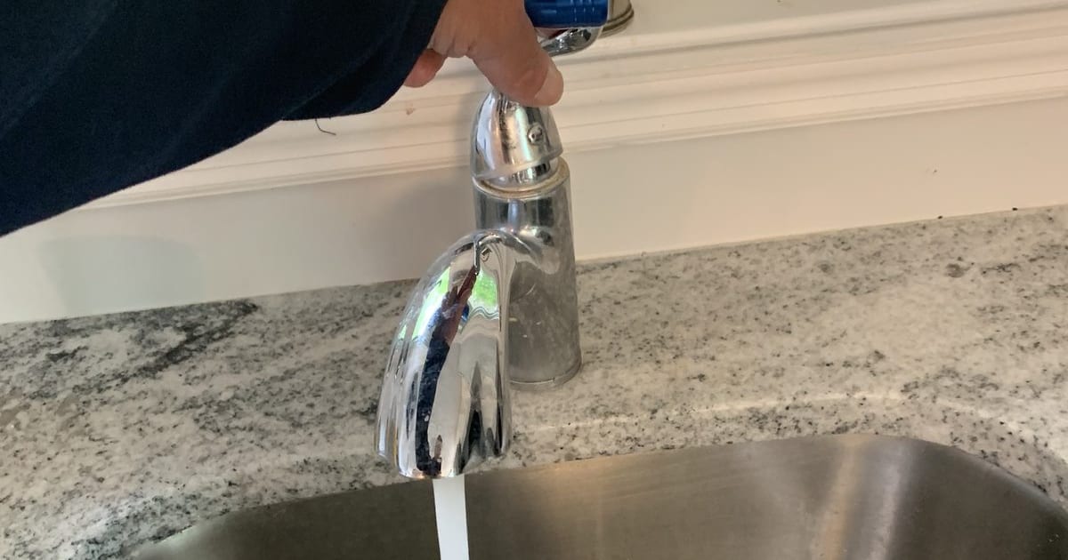 Close-up of a kitchen faucet with the sprayer head being removed.