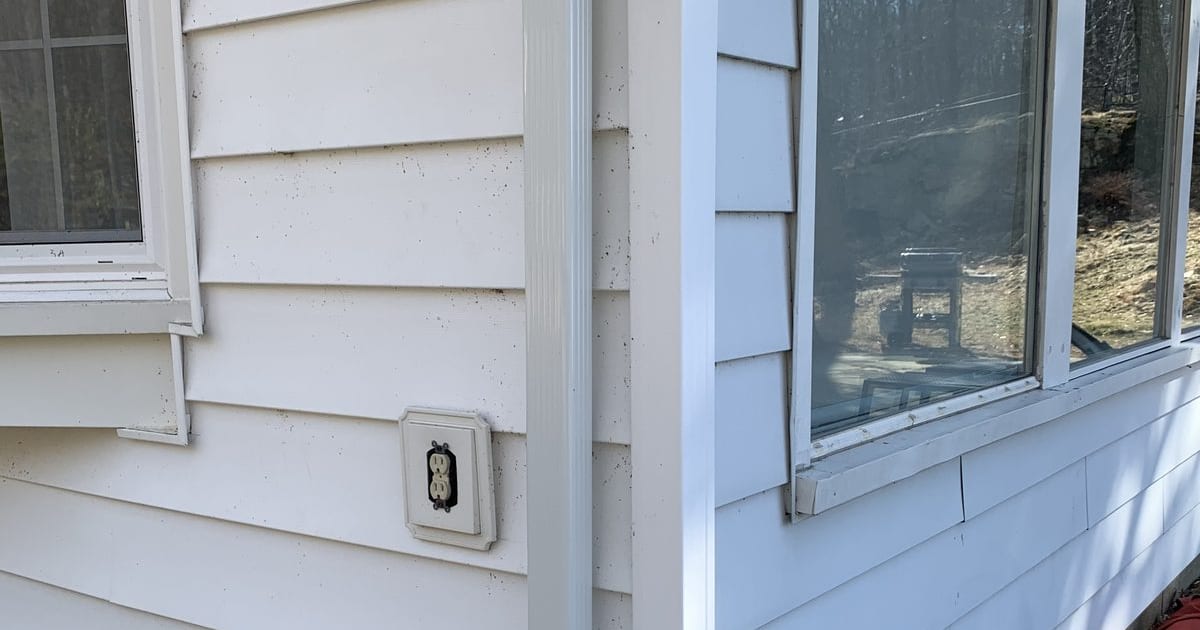 Outdoor spigot and downspout on a white-clapboard house exterior.