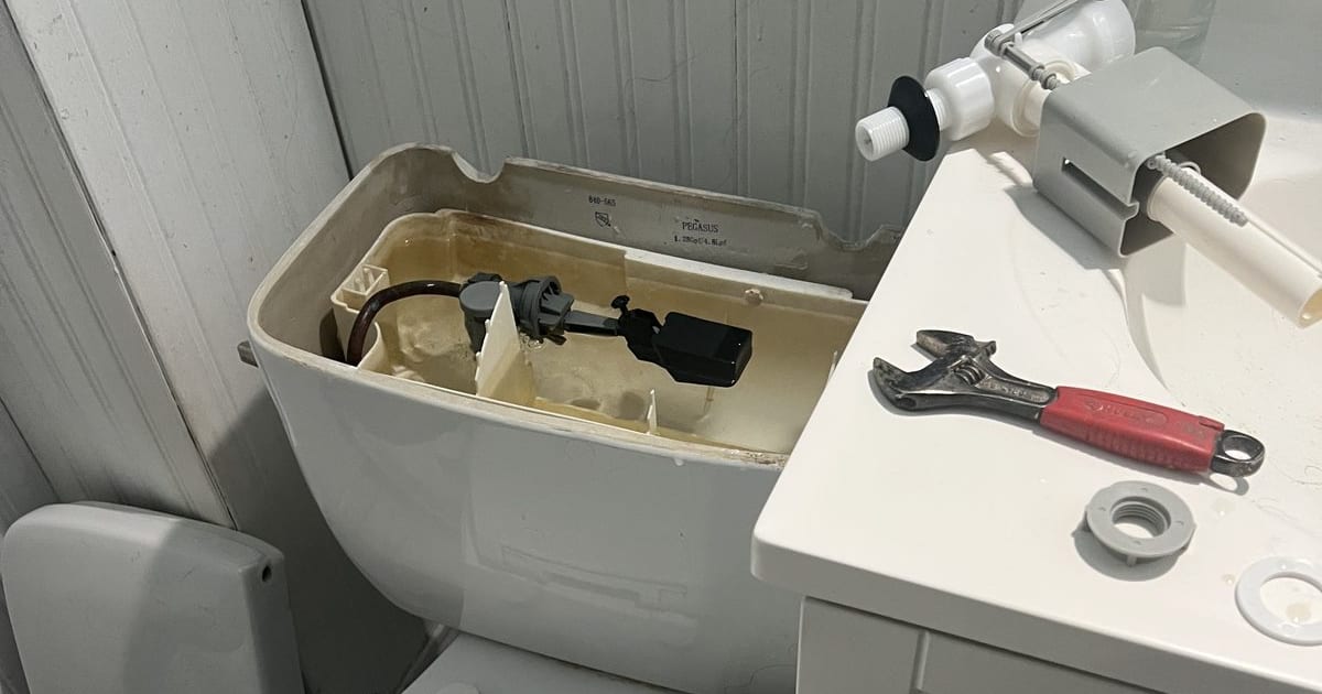 Toilet tank opened, showing the fill valve and flapper internals with a wrench nearby.