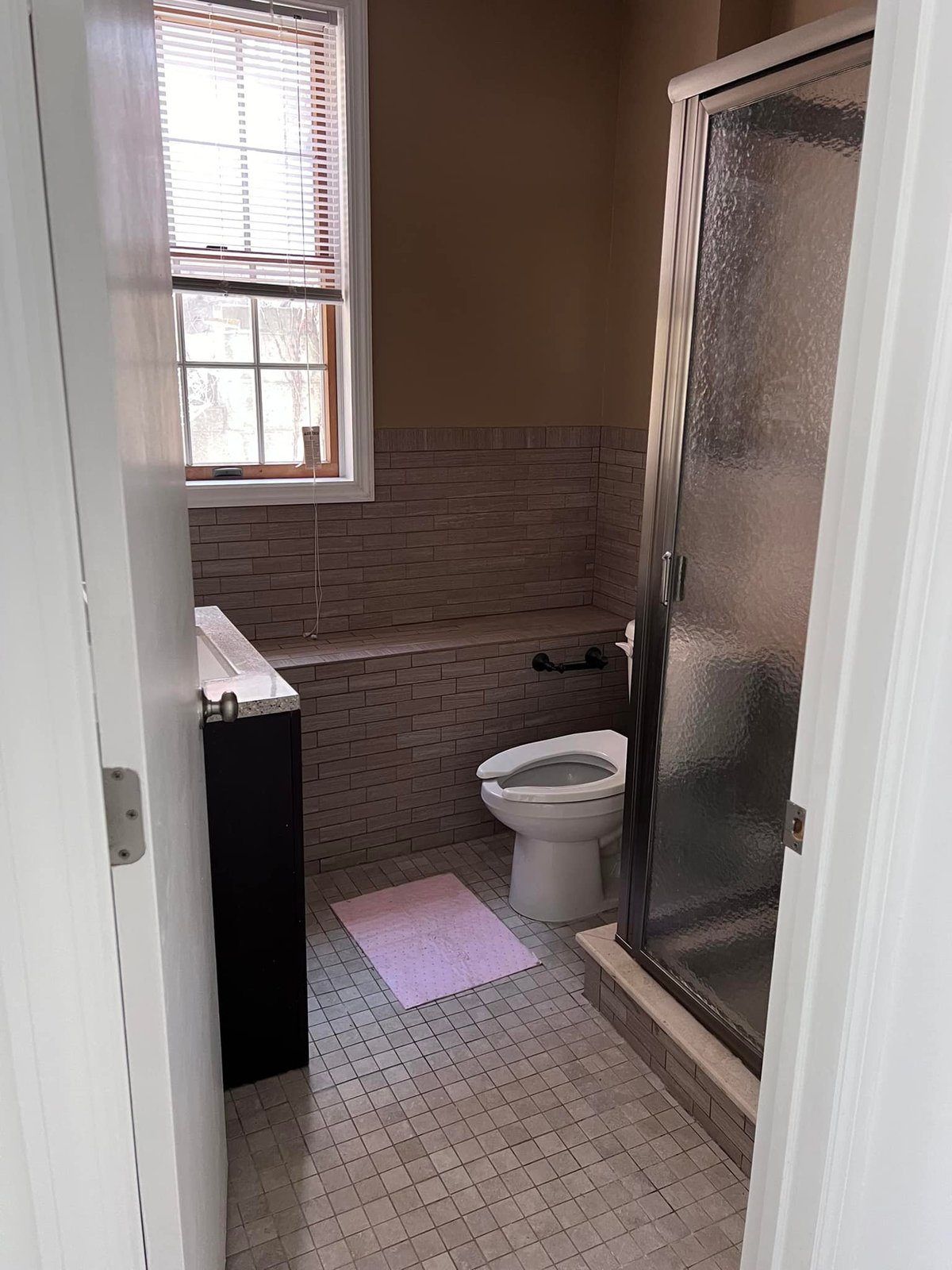 Brown tile, built-in tub surround, frosted shower stall — vintage and tired.