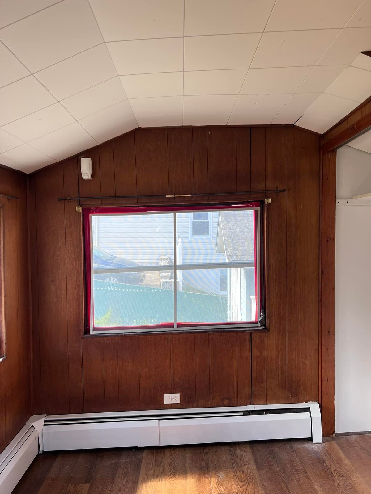 Empty bedroom with the dark paneling and drop ceiling still up. Heavy and dated.