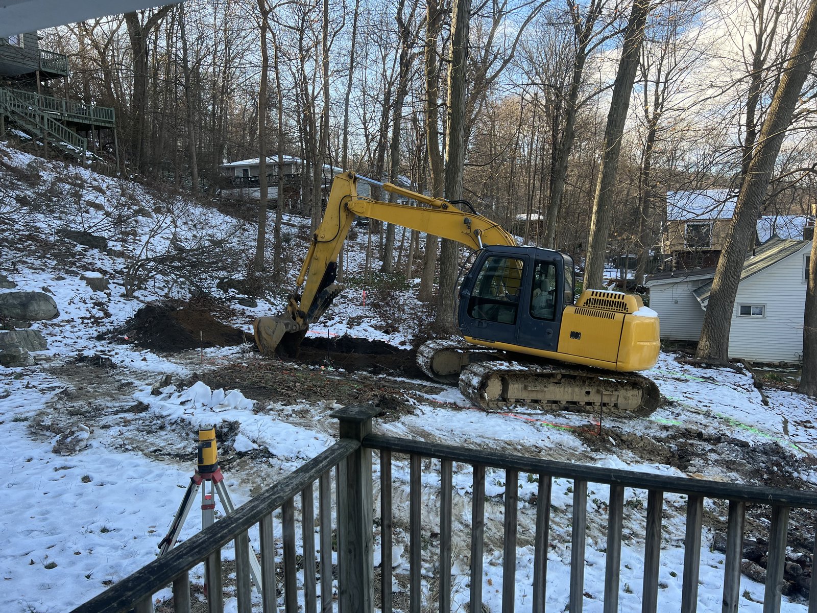 Surveyor's tripod on the snow while the excavator started the cut for the new tank.