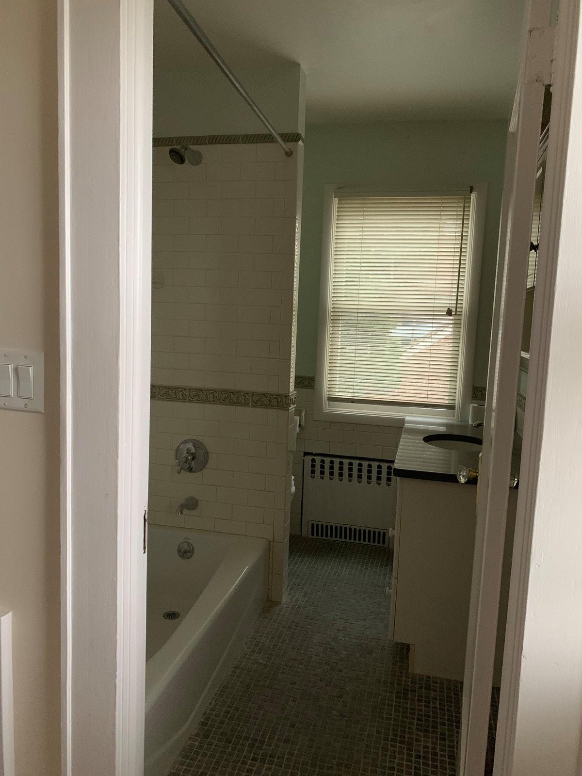 Original upstairs bath before — subway tile surround, mosaic floor, and a radiator under the window.