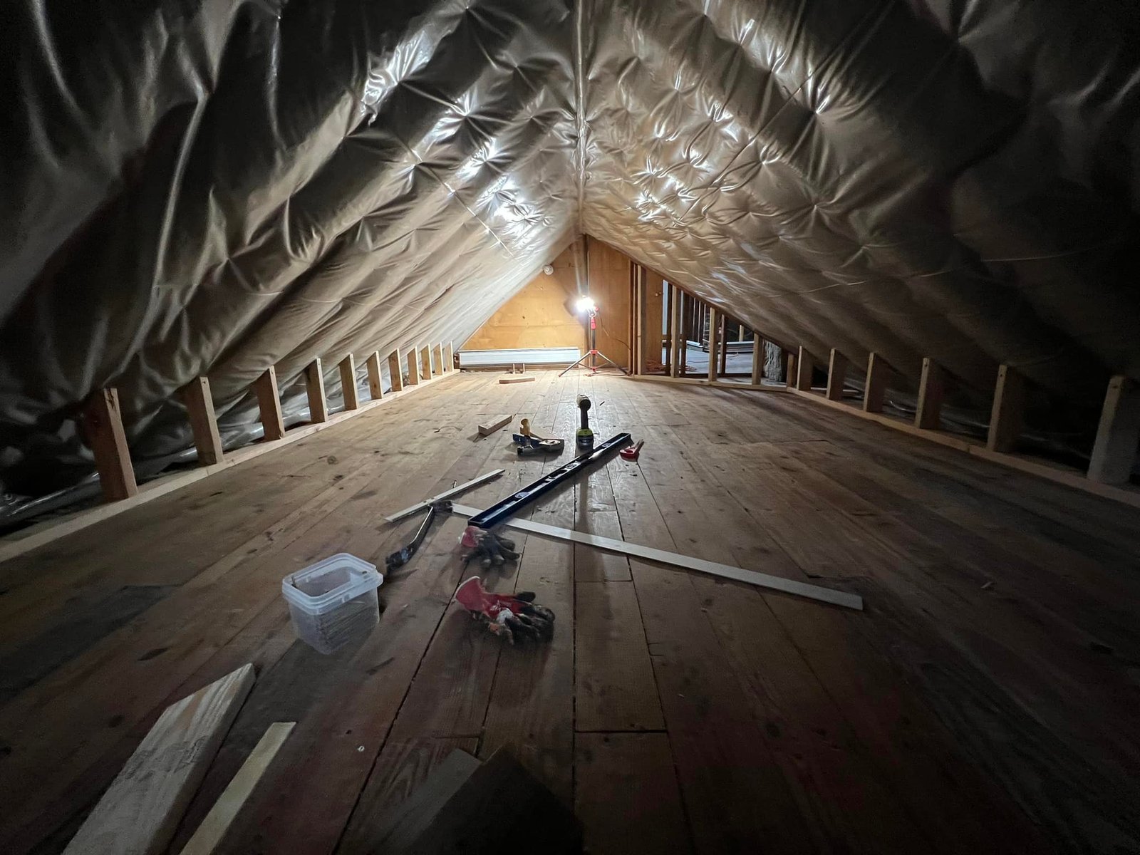 Radiant barrier going in under the rafters. Tools on the plank floor, no finished surfaces yet.