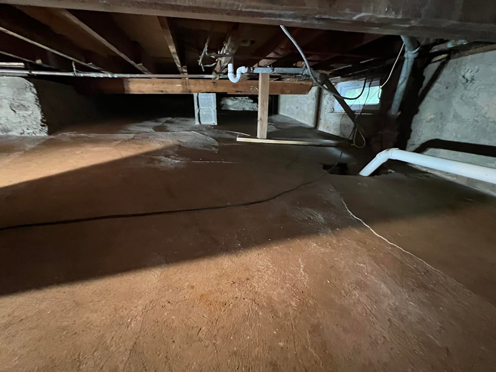 What I started with — dirt floor, joists hanging full of old plumbing and posts shimmed up on whatever was handy.