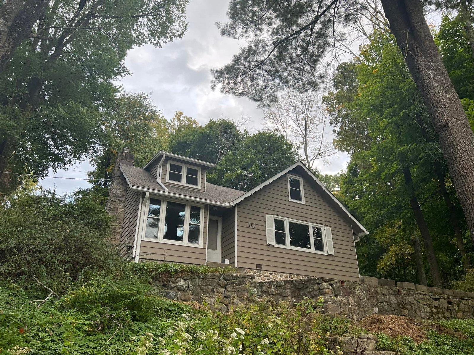 Wood-sided cottage on the stone retaining wall after the exterior work was done. Same house, holding itself differently.